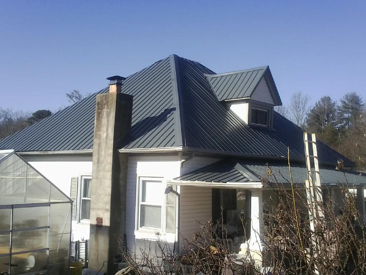 Dark blue standing seam metal roof on a white farmhouse with dormer — Slate & Tile Roof Repair by Roofing Brothers in Henrietta