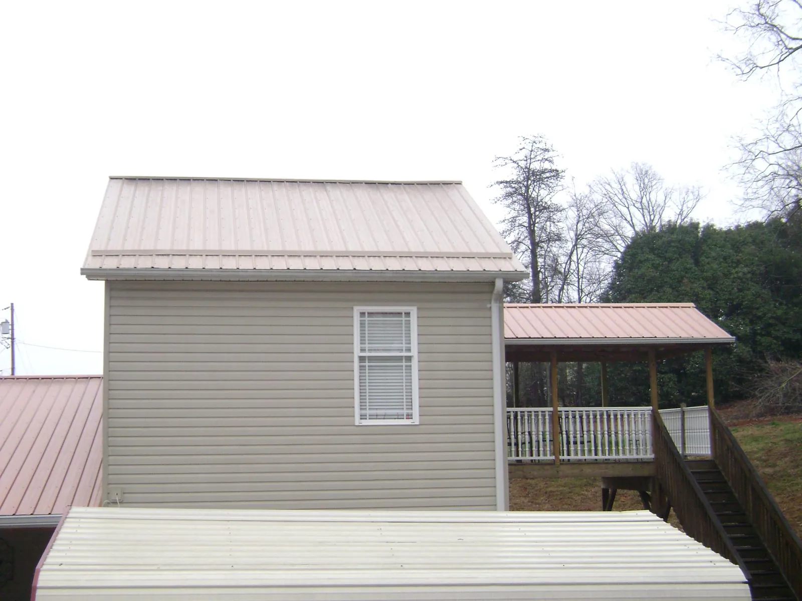 Tan metal roofs on a two story addition and attached porch, from a Roof Replacement job in Henrietta